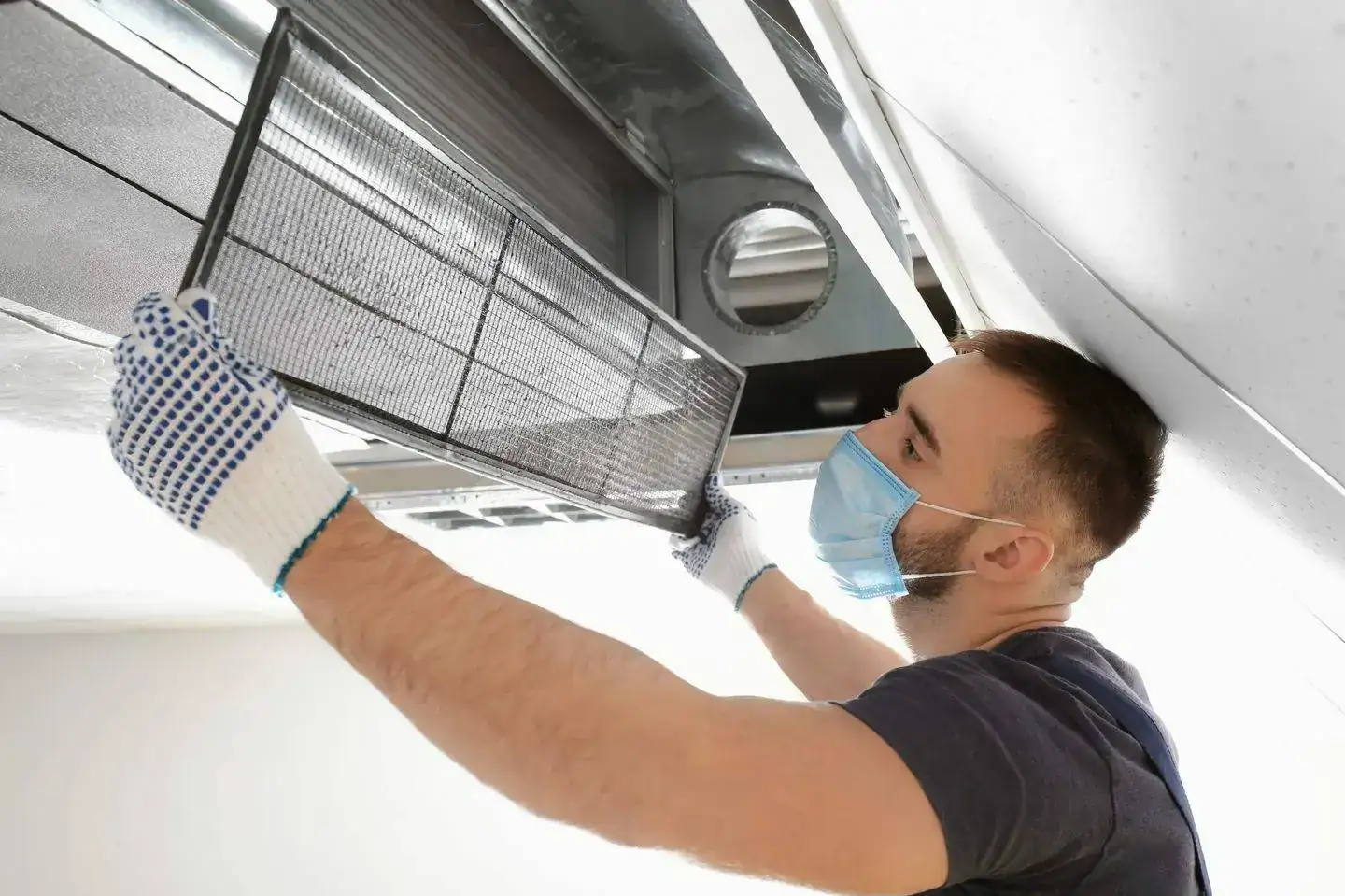 Technician in mask and gloves removing the filter from a ceiling AC unit, AC duct and filter cleaning services in Dubai by Limech