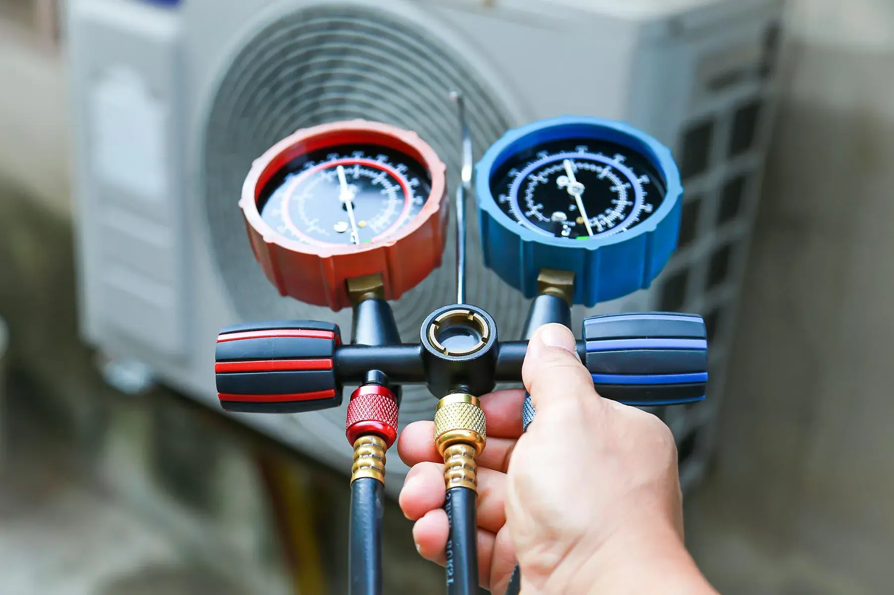 Technician holding refrigerant manifold gauges in front of an outdoor AC unit, AC gas refilling and leak check services in Dubai by Limech