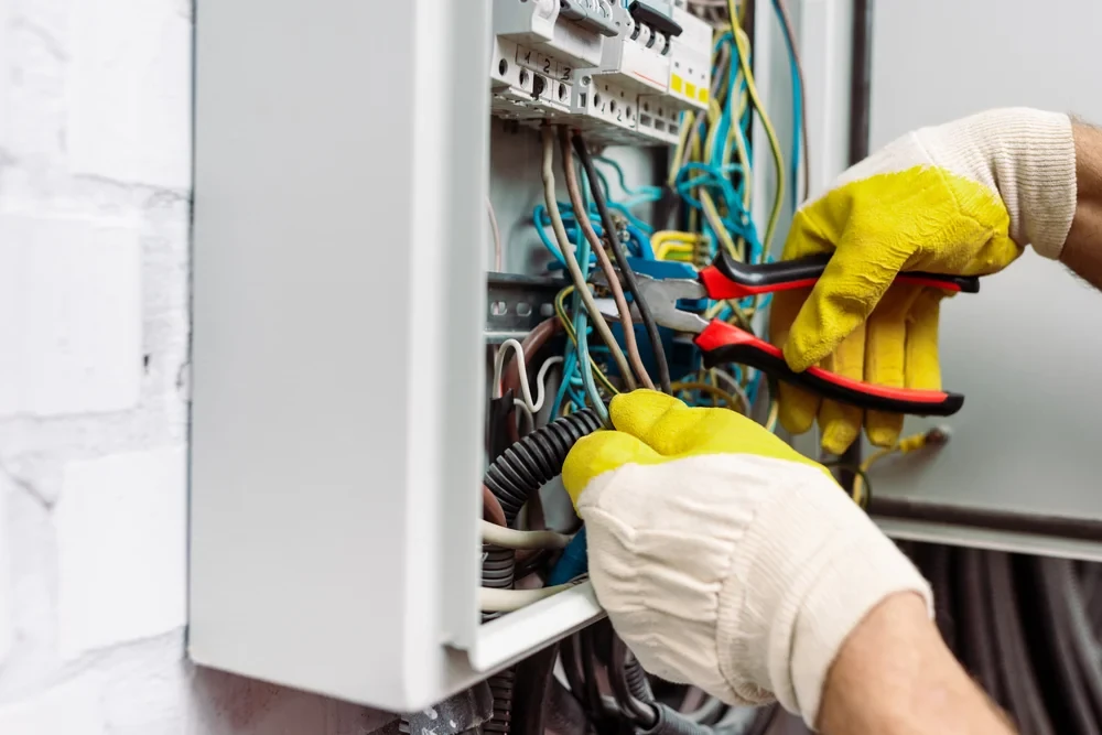 Electrician in work gloves using pliers to connect wires inside a distribution board, electrical wiring and repair services in Dubai by Limech