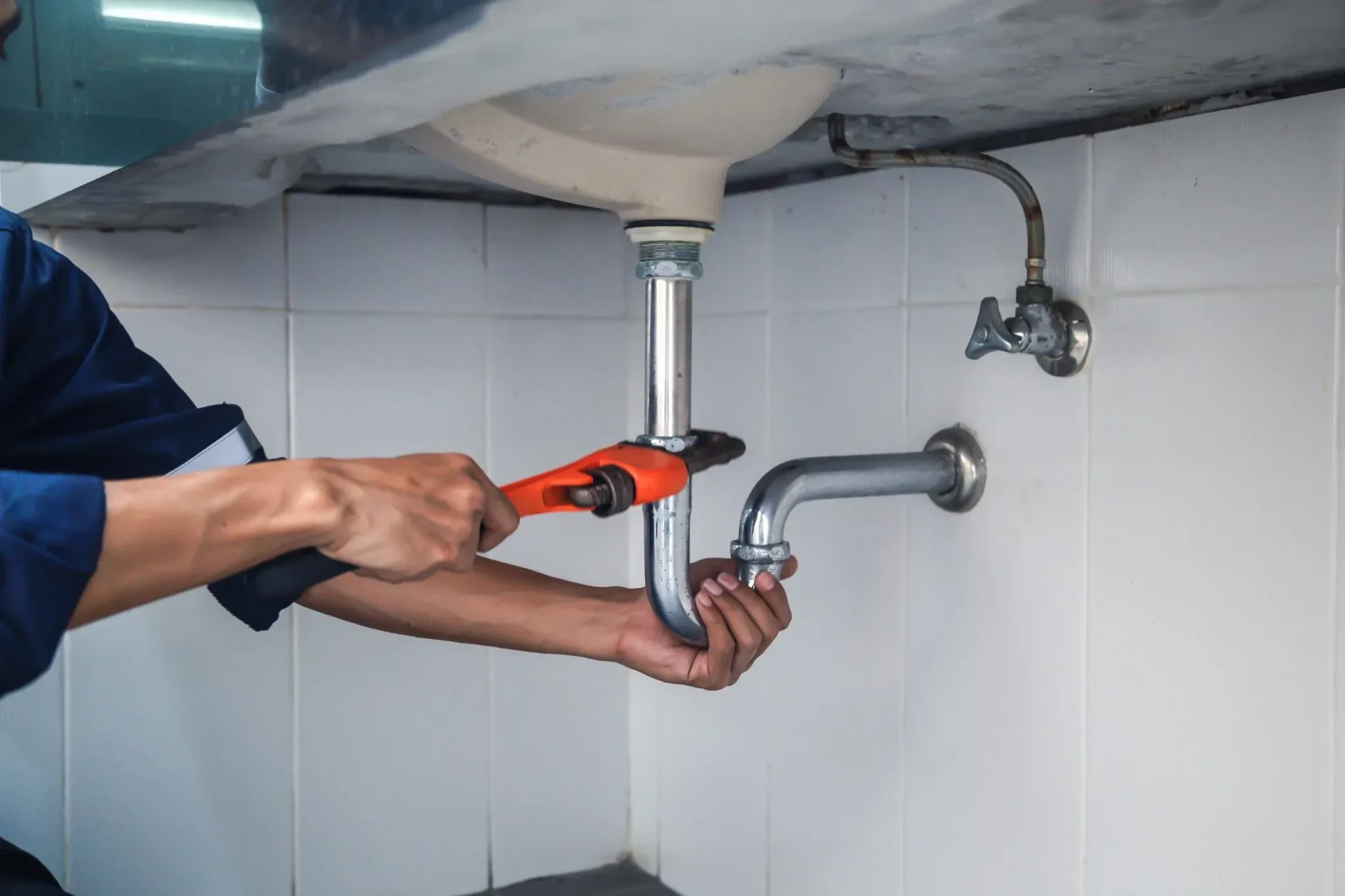 Plumber tightening a basin trap with a wrench to fix a leaking pipe, water leak repair and plumbing services in Dubai by Limech
